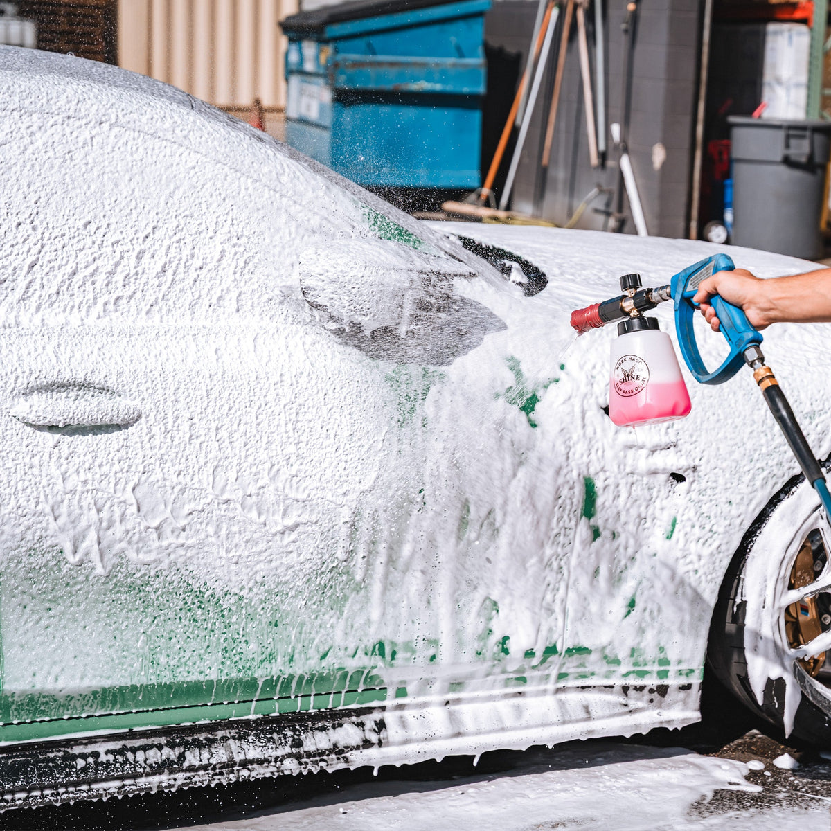 Detailer foaming the side of a green car with The Foam Thrower foam cannon and pink Shine Supply soap